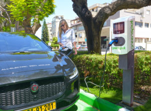 אישה מחברת יגואר חשמלית לעמדת טעינה של חברת גרינספוט