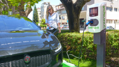 אישה מחברת יגואר חשמלית לעמדת טעינה של חברת גרינספוט