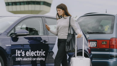 אישה עם טרולי עומדת לידר רכב חשמלי של פולקסווגן עם הכיתוב It's electric על הרכב