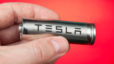 יד מחזיקה סוללה של חברת טסלה על רקע אדום