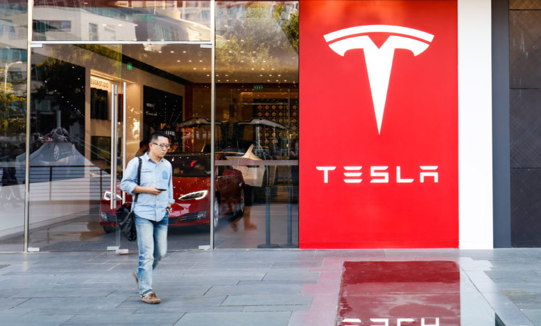 אדם יוצא מחנות של טסלה עם הלוגו של טסלה על אחד מקירות החנות באדום בסין