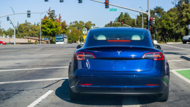 טסלה מודל 3 בצבע כחול עומד בצומת ברמזור אדום בקליפורניה