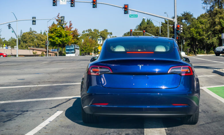 טסלה מודל 3 בצבע כחול עומד בצומת ברמזור אדום בקליפורניה