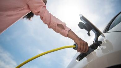 אישה מחברת רכב חשמלי לעמדת טעינה, צילום מלמטה