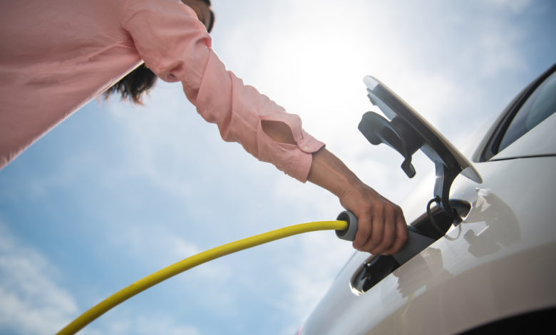 אישה מחברת רכב חשמלי לעמדת טעינה, צילום מלמטה