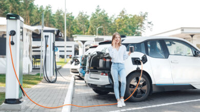 תחנת טעינה עם מספר רכבים חשמליים ואישה שעומדת ליד רכב ב.מ.וו המחובר לעמדת טעינה