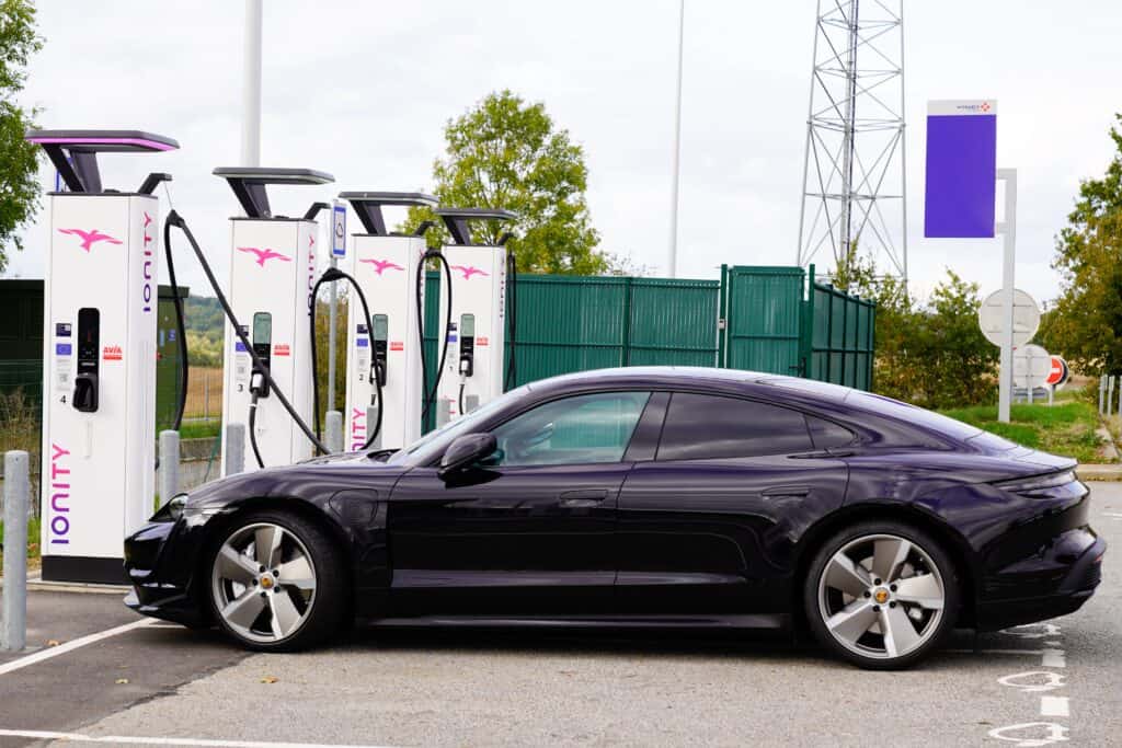 פורשה טייקן בצבע סגול מחוברת לעמדת טעינה בתחנה עם ארבעה מטענים מהירים של חברת IONITY בצרפת