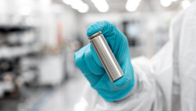 יד של אדם עם חליפה וכפפה מחזיקה תא גלילי של סוללה לרכב חשמלי במפעל החברה