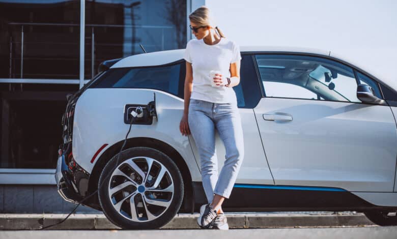 אשה עומד ליד רכב חשמלי של ב.מ.וו ומסתכלת על שקע הטעינה של הרכב בזמן טעינה