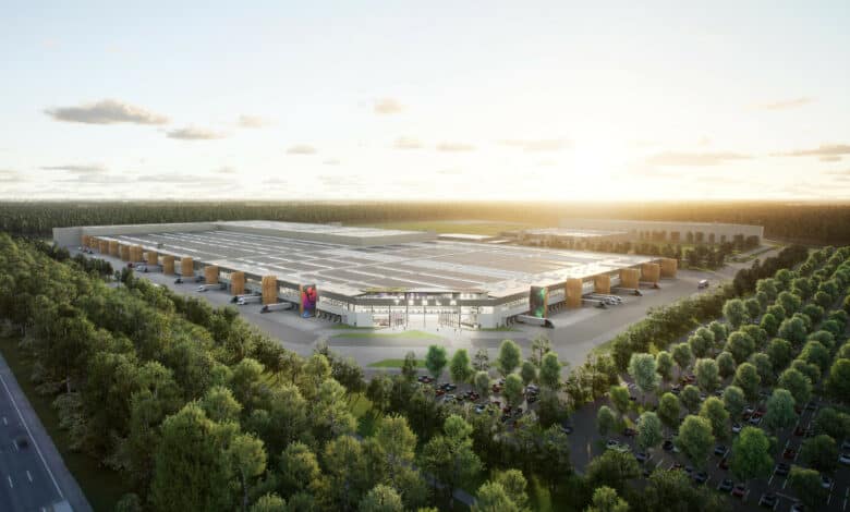 הדמיה של טסלה גיגה-פקטורי בברלין גרמניה, מוקף בעצים, ומשאיות טסלה סמי בחניון המפעל