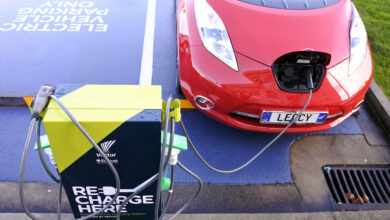 ניסאן ליף דור ראשון בצבע אדום עומדת באחת משתי חניות המיועדות לטעינת רכבים חשמליים ומחוברת לעמדה כפולה באוקלנד, ניו זילנד