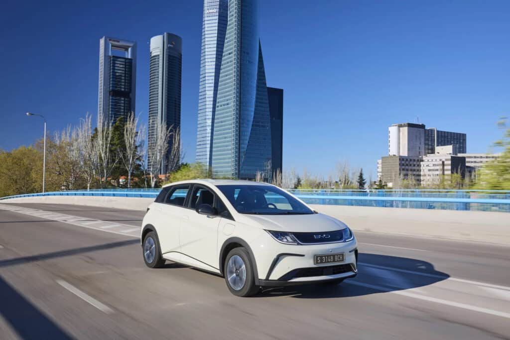 BYD דולפין לבנה בנסיעה על גשר עם רקע עירוני