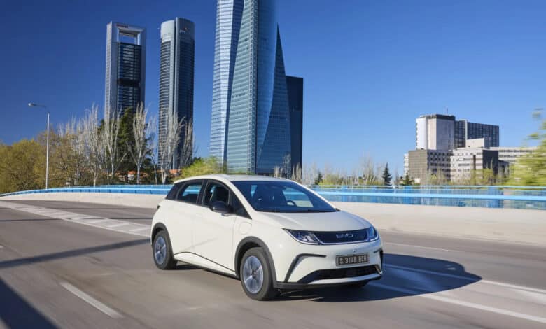 BYD דולפין לבנה בנסיעה על גשר עם רקע עירוני