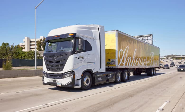 סמי טריילר מבית ניקולה מוטורס עם נגרר צהוב ועליו הכיתוב Anheuser-Busch בנסיעה בכביש מהיר בארצות הברית