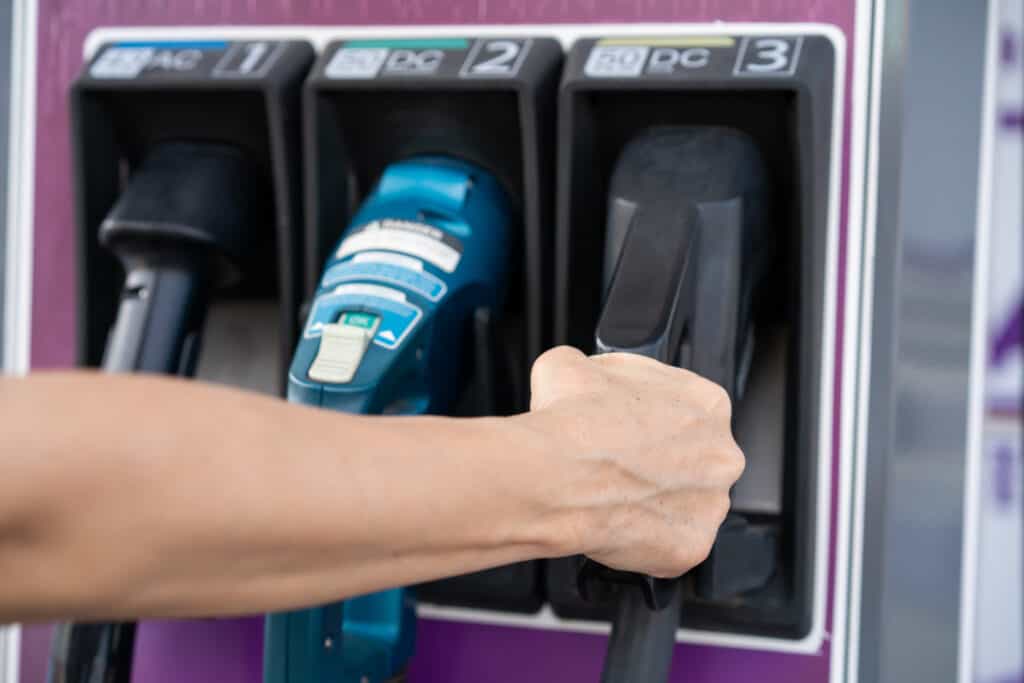 יד של אישה מחזיקה מחבר מסוג CCS2 של טעינה מהירה בעמדת טעינה של רכב חשמלי עם שלושה מחברים