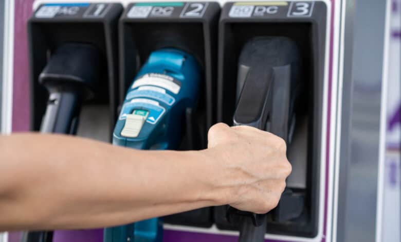 יד של אישה מחזיקה מחבר מסוג CCS2 של טעינה מהירה בעמדת טעינה של רכב חשמלי עם שלושה מחברים