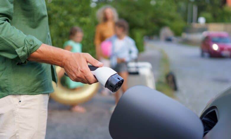 גבר מחזיק כבל טעינה עם מחבר Type2 לצורך חיבור לרכב חשמלי עם משפחות ברקע שממתינה לטעינה של הרכב