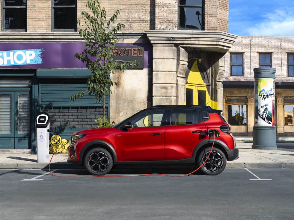 מבט צד על סיטרואן e-C3 חשמלית חונה בעיר ומחוברת לעמדת טעינה לרכב חשמלי