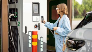 אישה משלמת באמצעות הפלאפון שלה בעמדת טעינה ציבורית לרכב חשמלי