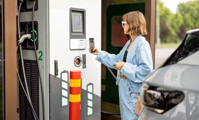 אישה משלמת באמצעות הפלאפון שלה בעמדת טעינה ציבורית לרכב חשמלי