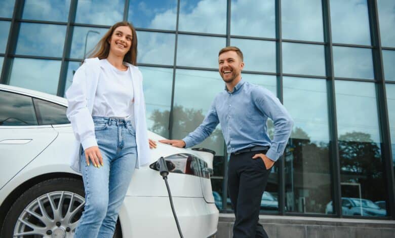 גבר ואישה עומדים לצד רכב חשמלי בזמן טעינה של הרכב