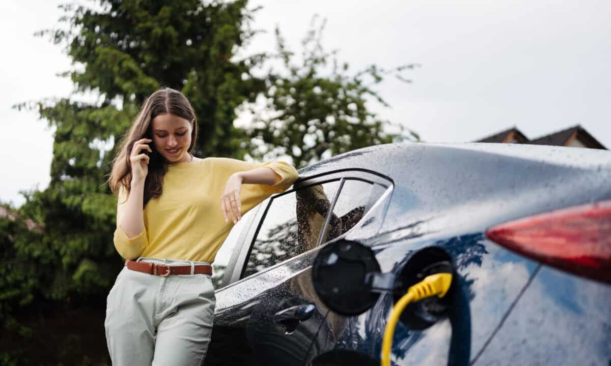 אישה מדברת בטלפון בזמן שהיא מטעינה רכב חשמלי ליד ביתה