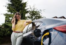 אישה מדברת בטלפון בזמן שהיא מטעינה רכב חשמלי ליד ביתה