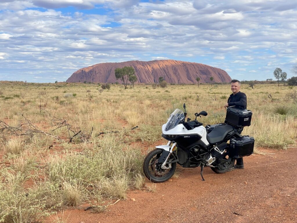 רומן עומד ליד האופנוע החשמלי שלו על רקע נופי הטבע המרהיבים של אוסטרליה, במהלך מסע הרכיבה שלו מסביב לעולם