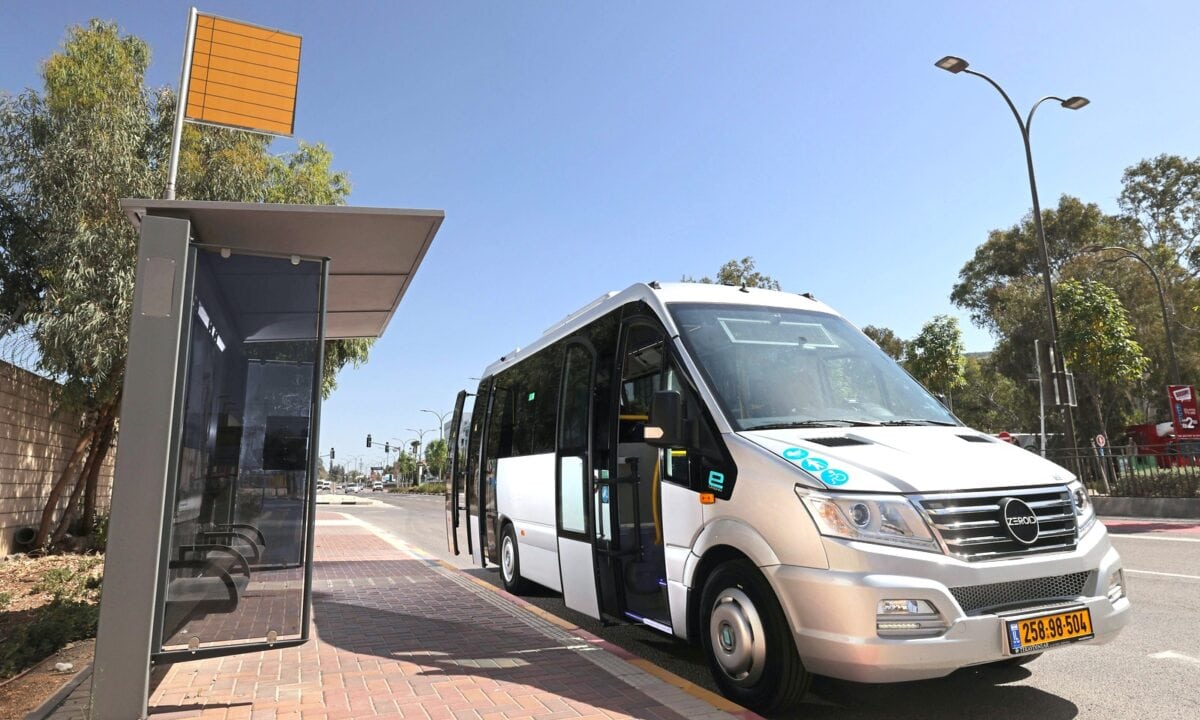 מיניבוס חשמלי בצבע אפור כסוף בהיר של QEV עומד לצד תחנת אוטובוס בירושלים