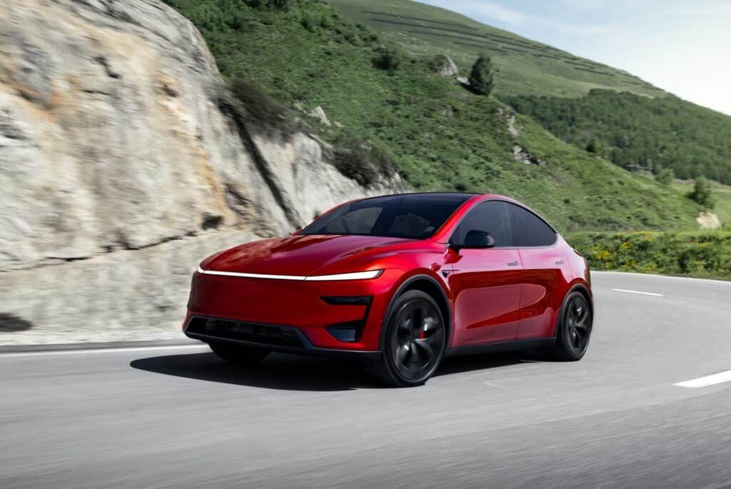 טסלה מודל Y פרפורמנס אדומה בנסיעה על כביש ההררי מפותל בין הרים ירוקים